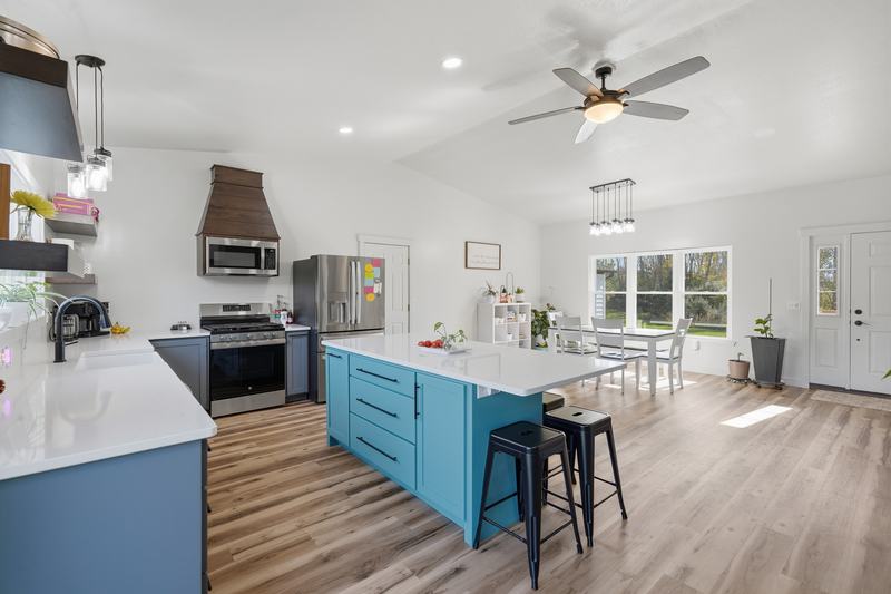 Bright open kitchen with a teal island, quartz counters and a wood range hood