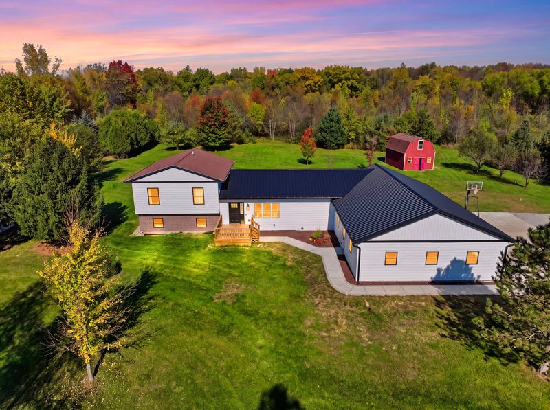 Aerial twilight photo of a farmhouse and red barn on a wooded lot at sunset