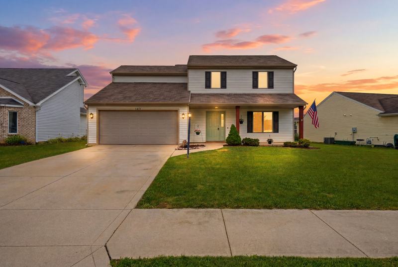 Two-story home at dusk with glowing windows and a pastel sunset sky